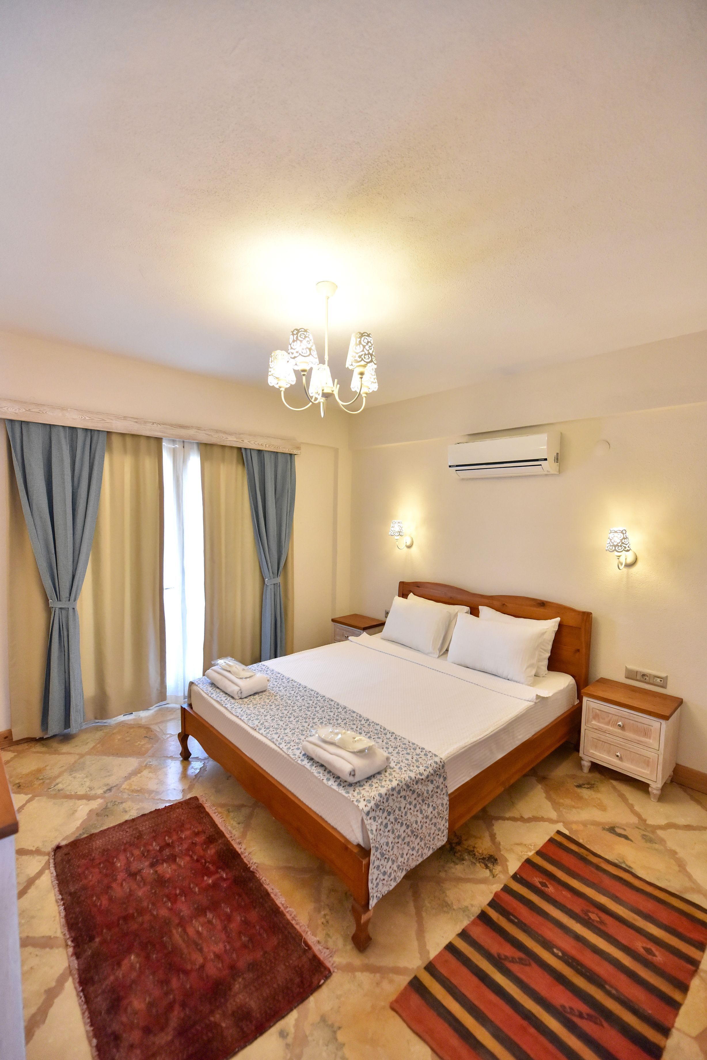 Una habitación de hotel con una cama grande, dos mesitas de noche, un candelabro y un equipo de aire acondicionado.