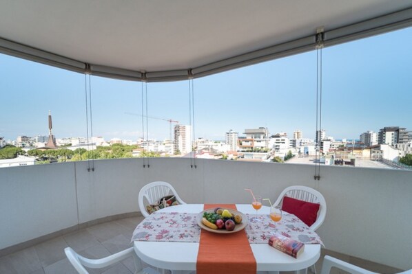 A balcony with a table set for two, a fruit bowl, and a drink on the table.