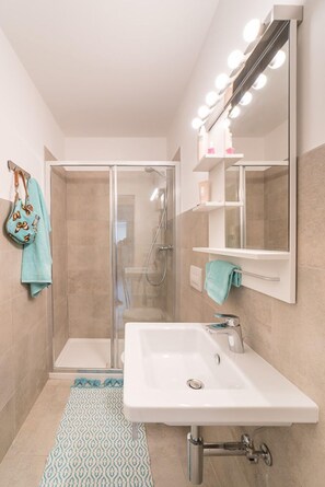 Un baño moderno con cabina de ducha de vidrio, un lavabo blanco y un espejo grande con iluminación.