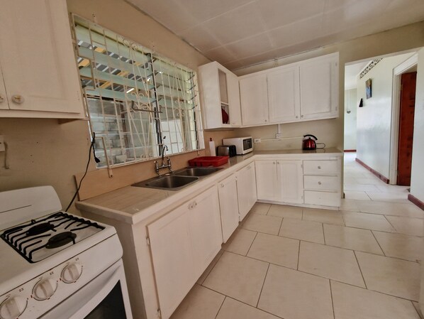 A kitchen with white cabinets, a gas stove, a microwave, and a red kettle. - Family-friendly home from home located close to beach, bars and restaurants (Bridgetown)