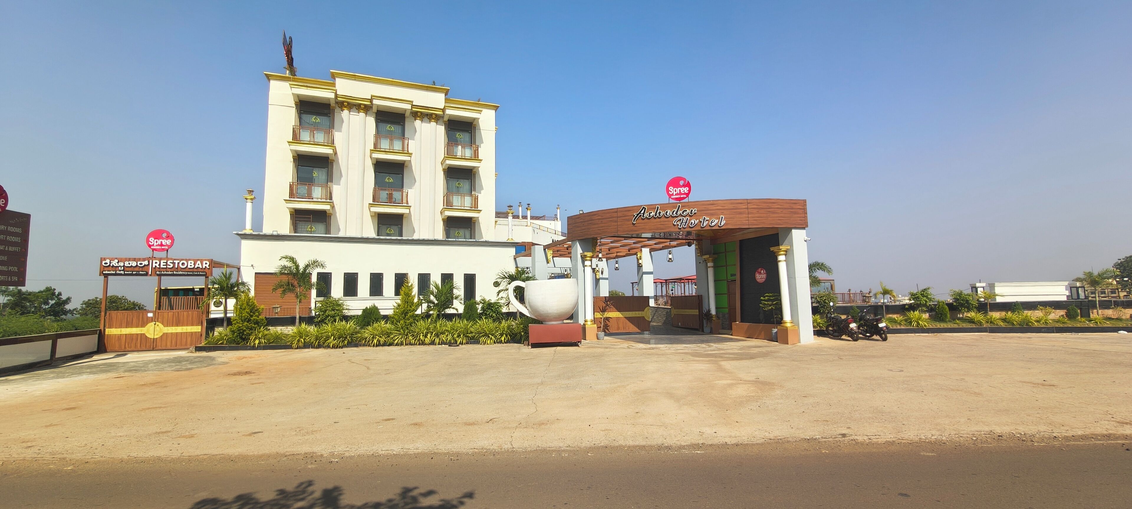 A hotel entrance with a large sign, a gated entrance, and a parking area.
