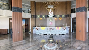A reception area with a wooden reception desk, a sunburst design on the wall, and a statue above the desk. - Spree Ashodev Hotel (Bidar)