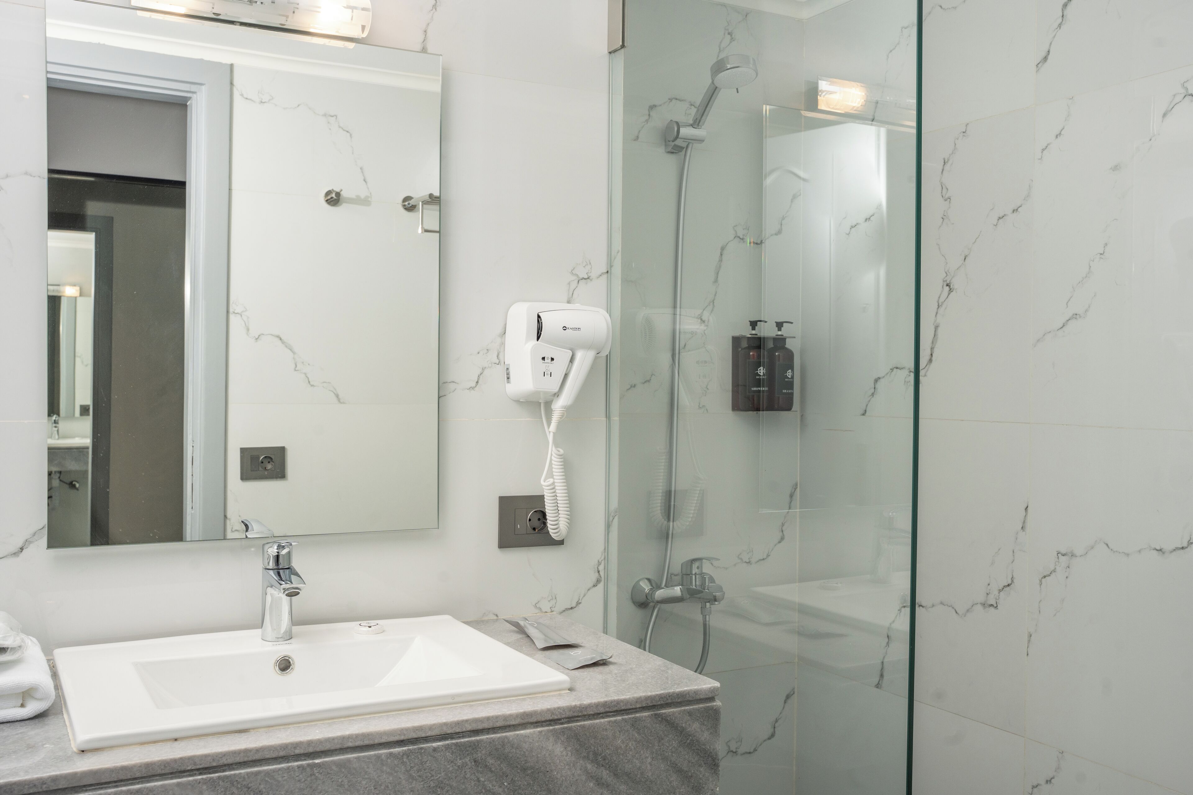 A modern bathroom with a white sink, a hairdryer, and a glass-enclosed shower.