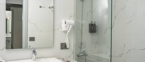 A modern bathroom with a white sink, a hairdryer, and a glass-enclosed shower.