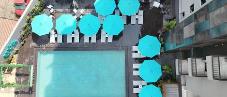 An aerial view of a rooftop pool area with multiple blue umbrellas and white lounge chairs arranged around it.