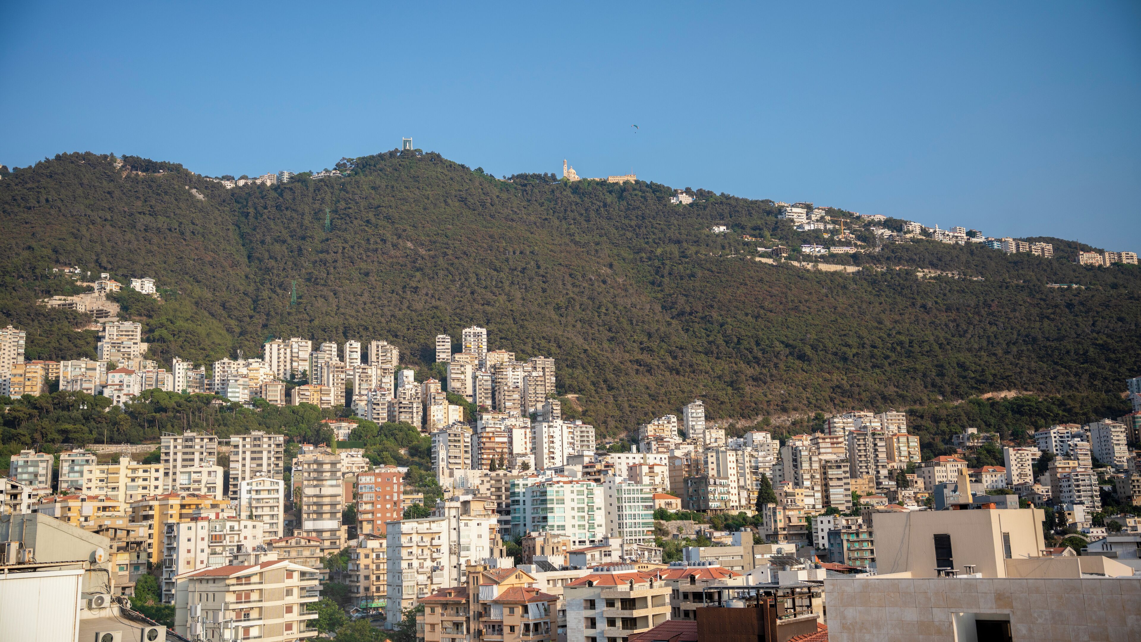 A densely packed urban area with numerous high-rise buildings, a prominent hill with a tower in the background, and a clear sky.