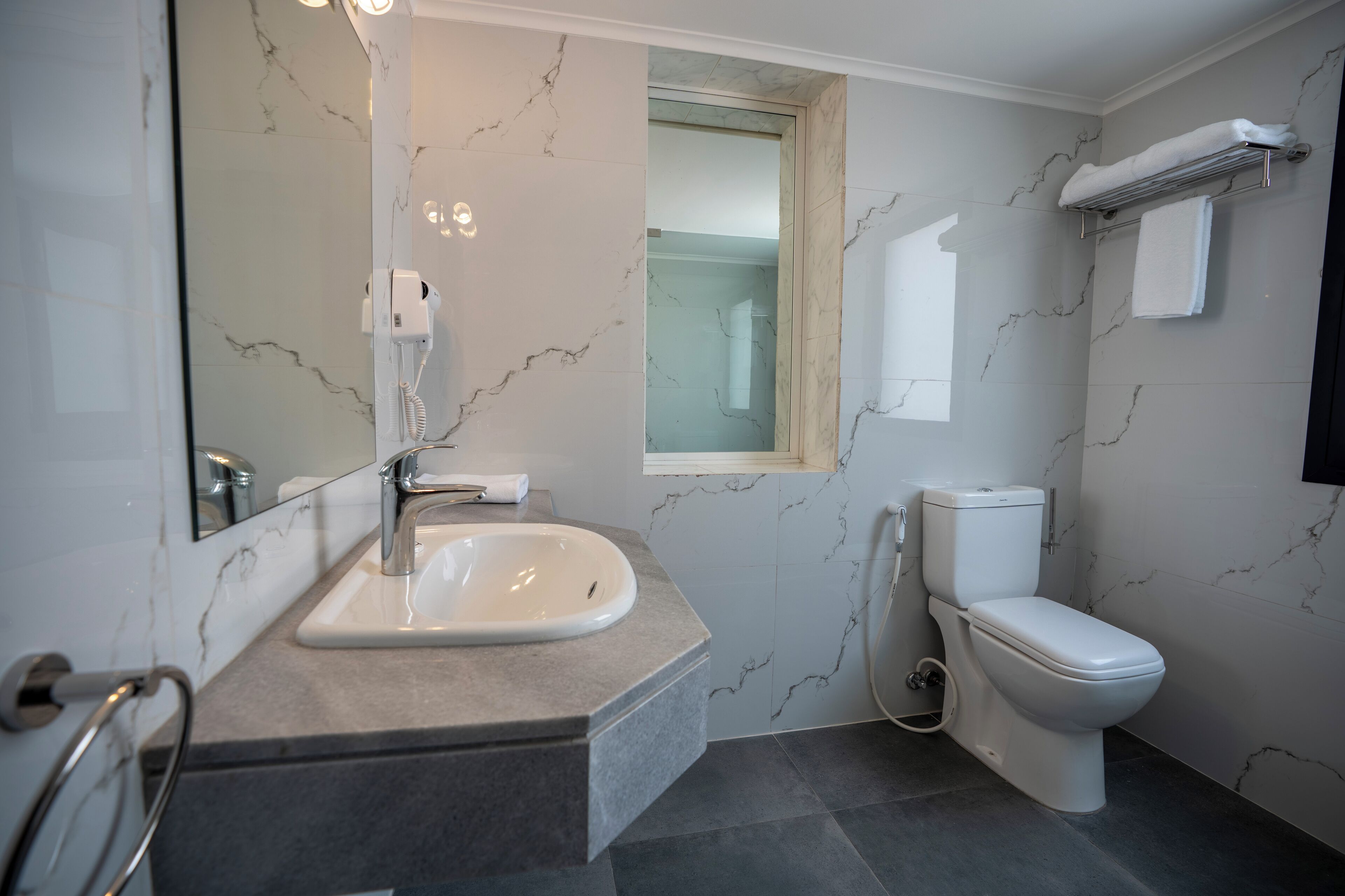 A modern bathroom with a marble sink, a toilet, and a towel rack.