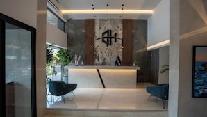 A modern reception area with a marble wall, a reception desk, and two blue chairs. - Beverly Beach Hotel (Jounieh)