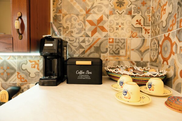 Una encimera de cocina con una cafetera, un depósito de café y tazas decorativas.