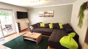 Un salón con un sofá seccional, una mesa de centro, un televisor de pantalla plana y un radiador.