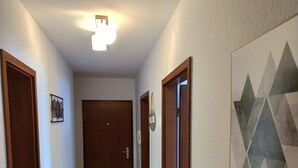 Un pasillo con suelo de madera, una lámpara en el techo y una obra de arte geométrica en la pared.