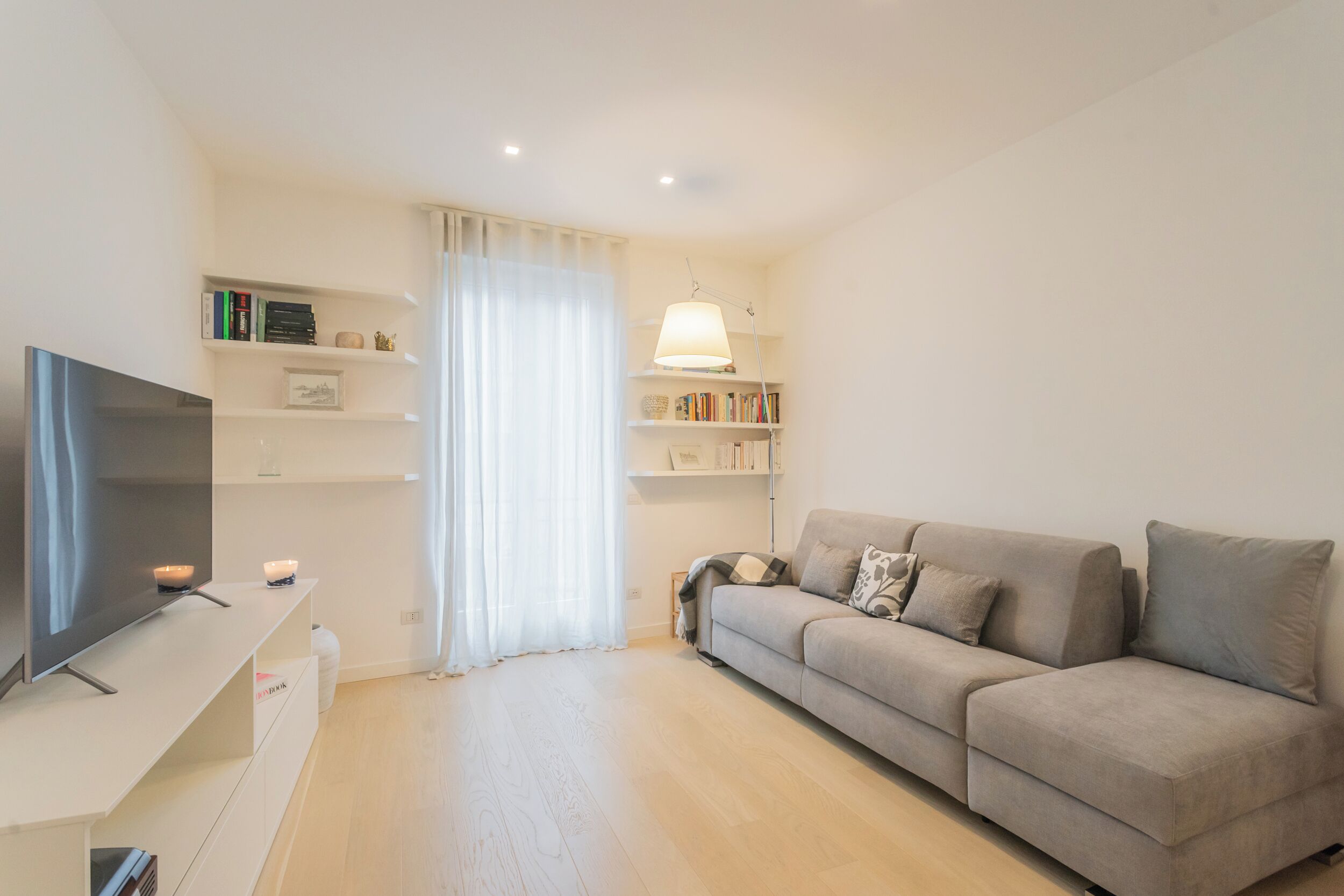 A modern living room with a flat-screen TV, a sofa, and a bookshelf.