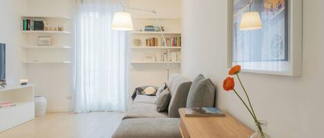 A modern living room with a sofa, a wooden side table, a bookshelf, and a painting on the wall.