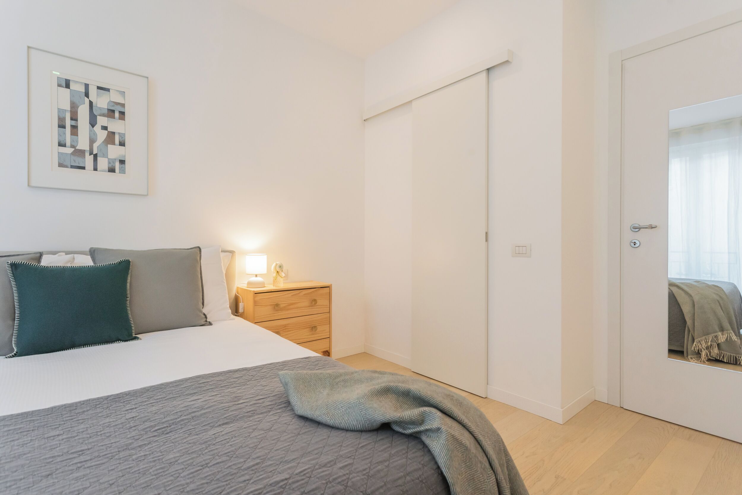 Un dormitorio con cama, mesita de noche, lámpara y una puerta corredera.