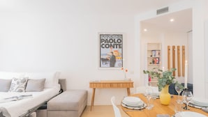 A modern living room with a sofa, a dining table set for two, and a poster on the wall. - Central & White Apartment by Rent all Como (Como)