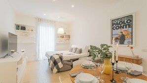 A modern, well-lit room with a bed, a dining table set for two, a TV, and a bookshelf. - Central & White Apartment by Rent all Como (Como)