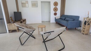 A living room with a blue sofa, two folding chairs, a small round table, and a television on a wooden stand.