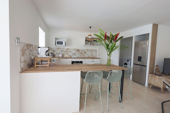 A modern kitchen with a wooden island, bar stools, a microwave, and a refrigerator.