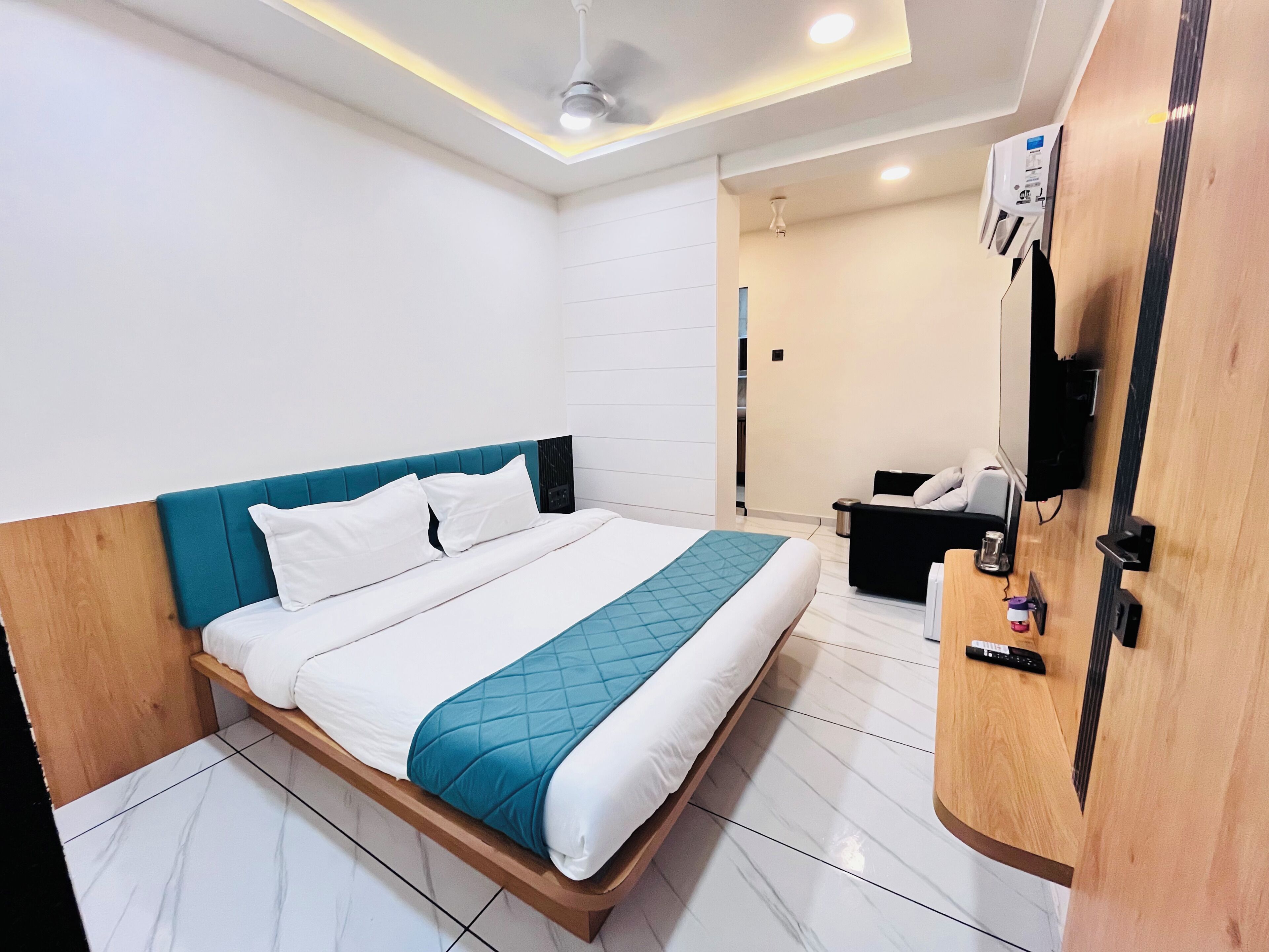 Una habitación de hotel moderna con una cama, un cabecero de madera, una mesita de noche, un televisor y un ventilador de techo.