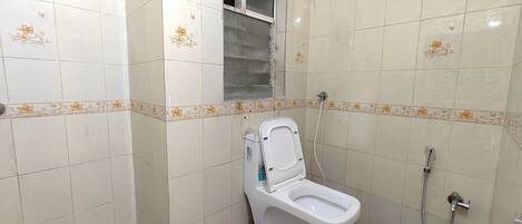 A small bathroom with a toilet, a shower, and a window.