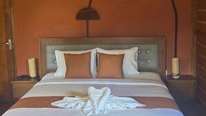 Un lit bien fait, avec une couette blanche et deux oreillers, une tête de lit en bois, une lampe de chevet et un luminaire fixé au mur.