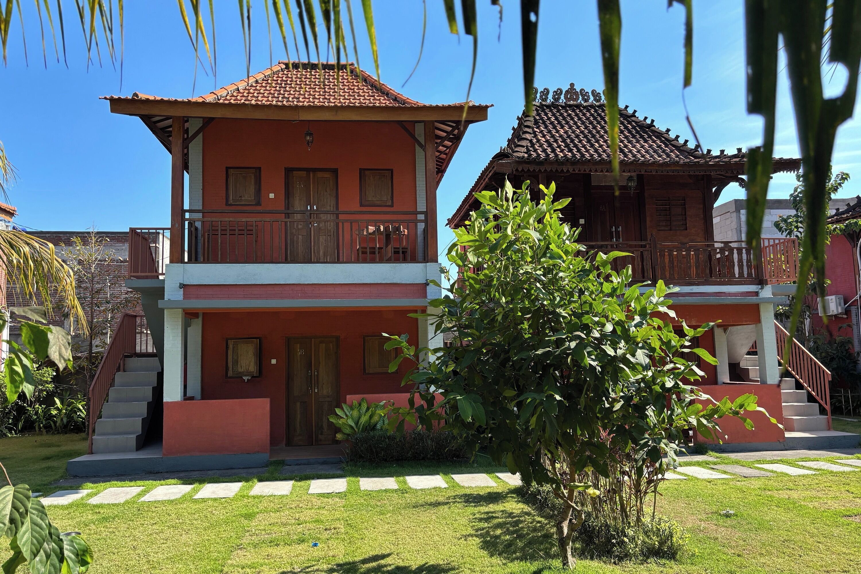 A two-story building with a red facade and a tiled roof, featuring a balcony on the upper floor.