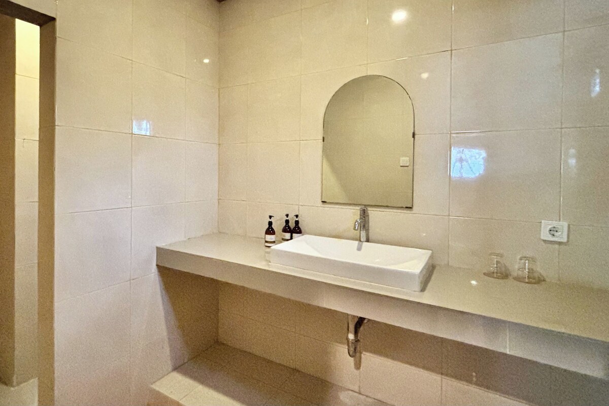 A modern bathroom with a white sink, a large mirror, and a tiled wall.