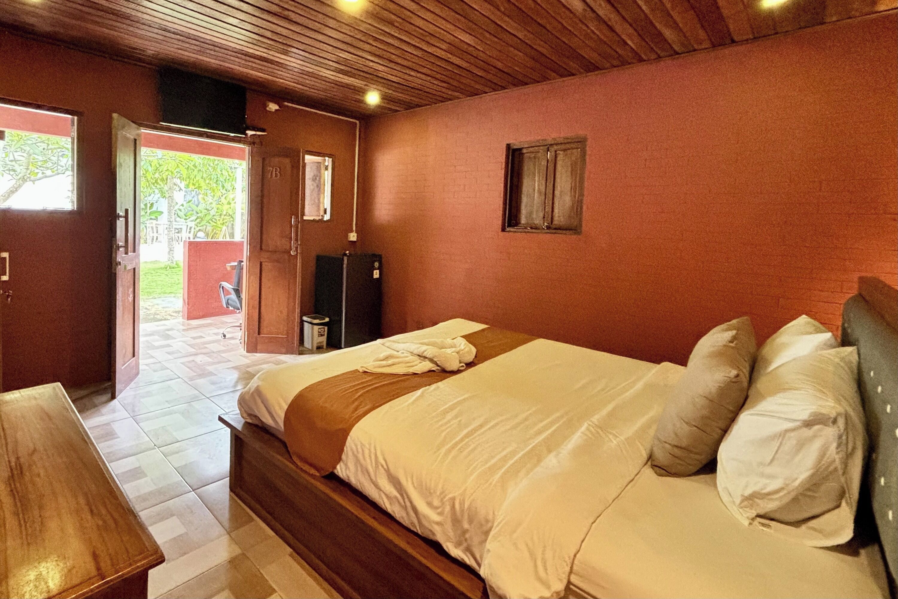 Un dormitorio con una cama de madera, un banco y una puerta que da a un área exterior.
