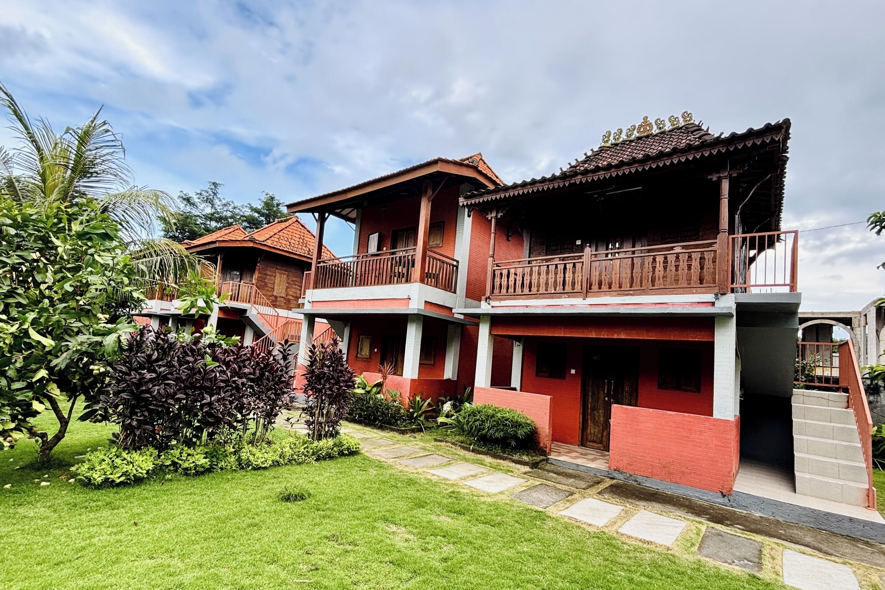 A two-story building with a red and grey facade, balconies, and a garden area.