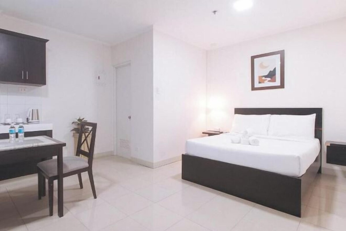 A hotel room with a bed, a desk with a chair, a small table, and a picture on the wall.