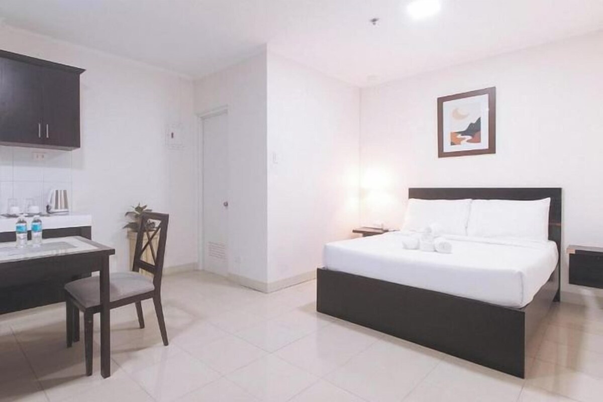 A hotel room with a bed, a desk with a chair, a small table, and a picture on the wall.