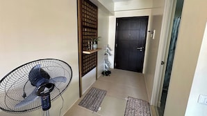 A hallway with a standing fan, a dark door, and a small shelf with plants. - Avida Units Staycation near Ayala Serin Tagaytay (Tagaytay)