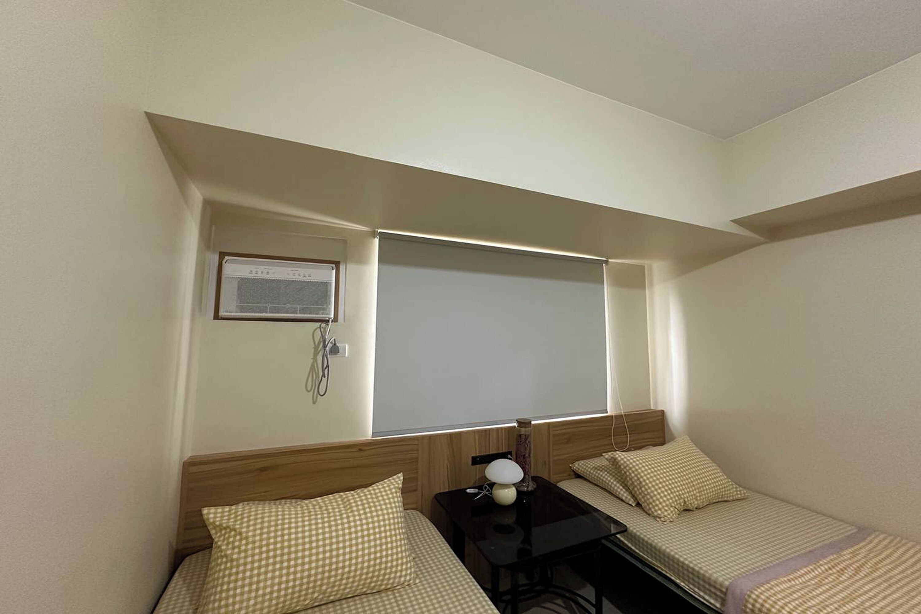 A small, compact room with two single beds, a small table, and a desk.