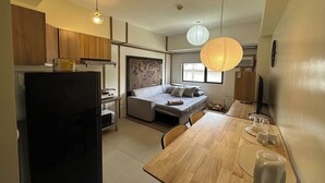 A compact kitchen with a refrigerator, wooden cabinets, a dining table, and a sofa. - Avida Units Staycation near Ayala Serin Tagaytay (Tagaytay)