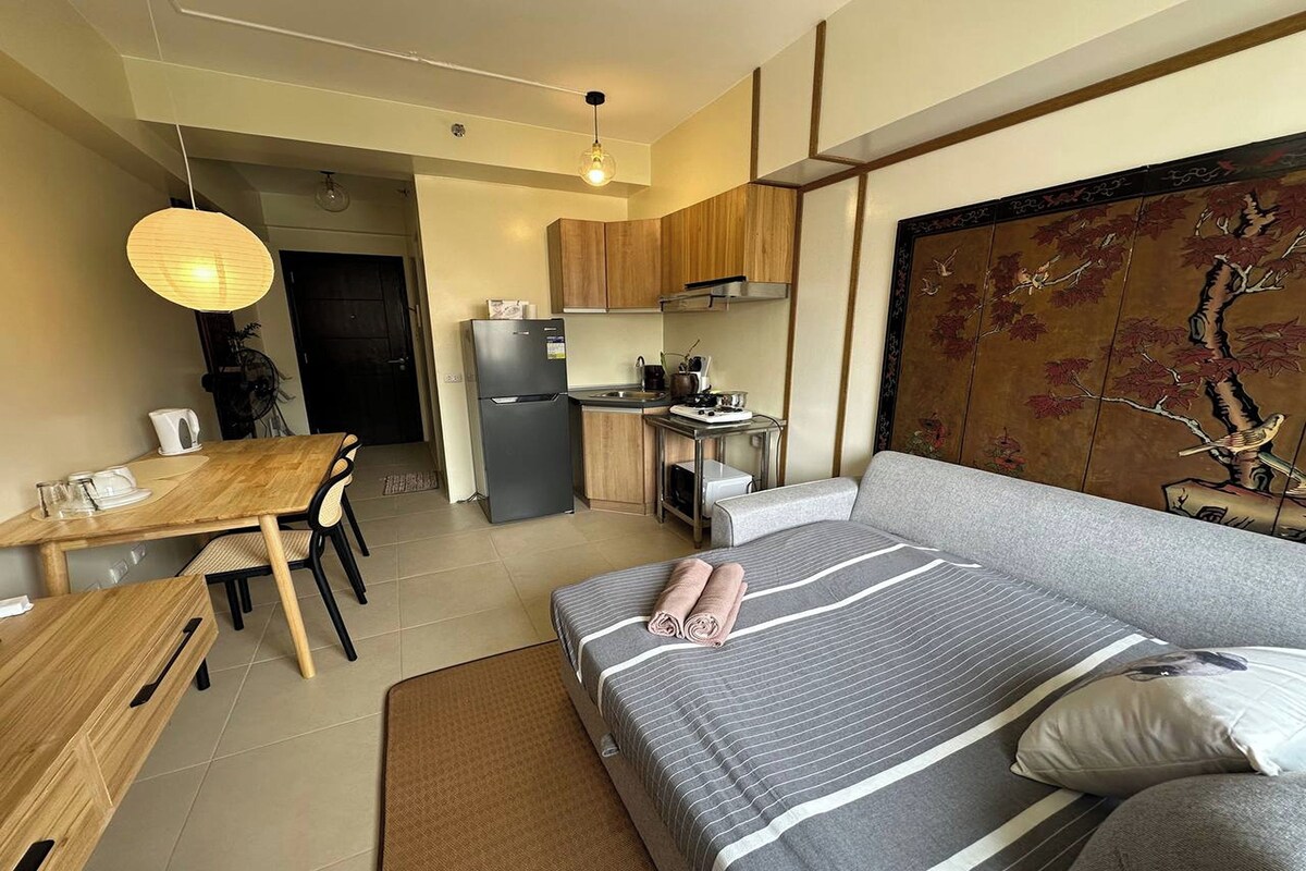 Une chambre d’hôtel compacte comprenant un lit, une table à manger, un coin cuisine et un grand élément décoratif mural.