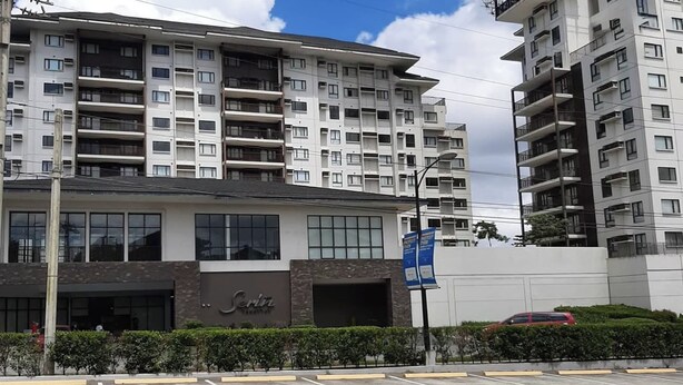 A multi-story hotel with a modern facade, large windows, and a parking lot in front. - Avida Units Staycation near Ayala Serin Tagaytay (Tagaytay)