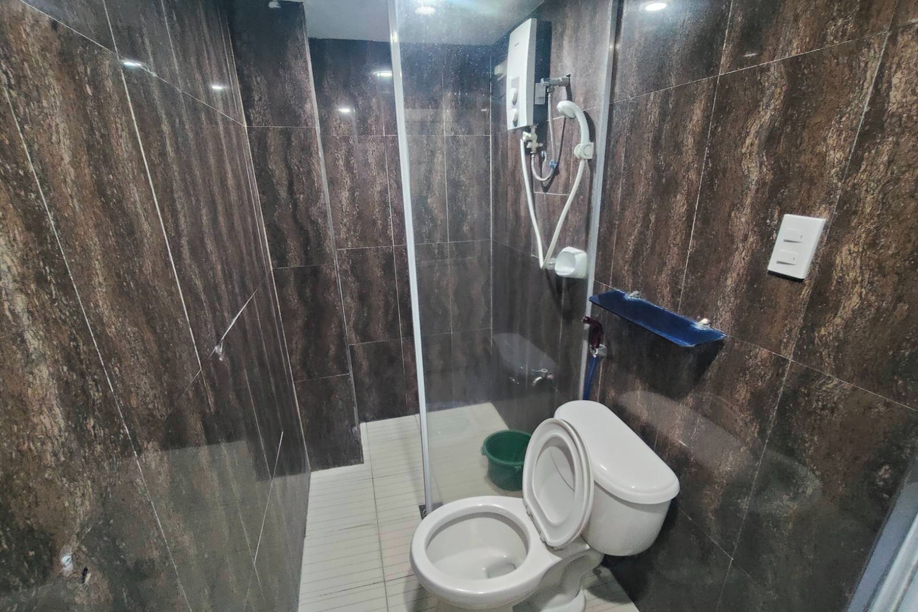 Et moderne badeværelse med en brusekabine i glas, et hvidt toilet og en grøn spand.