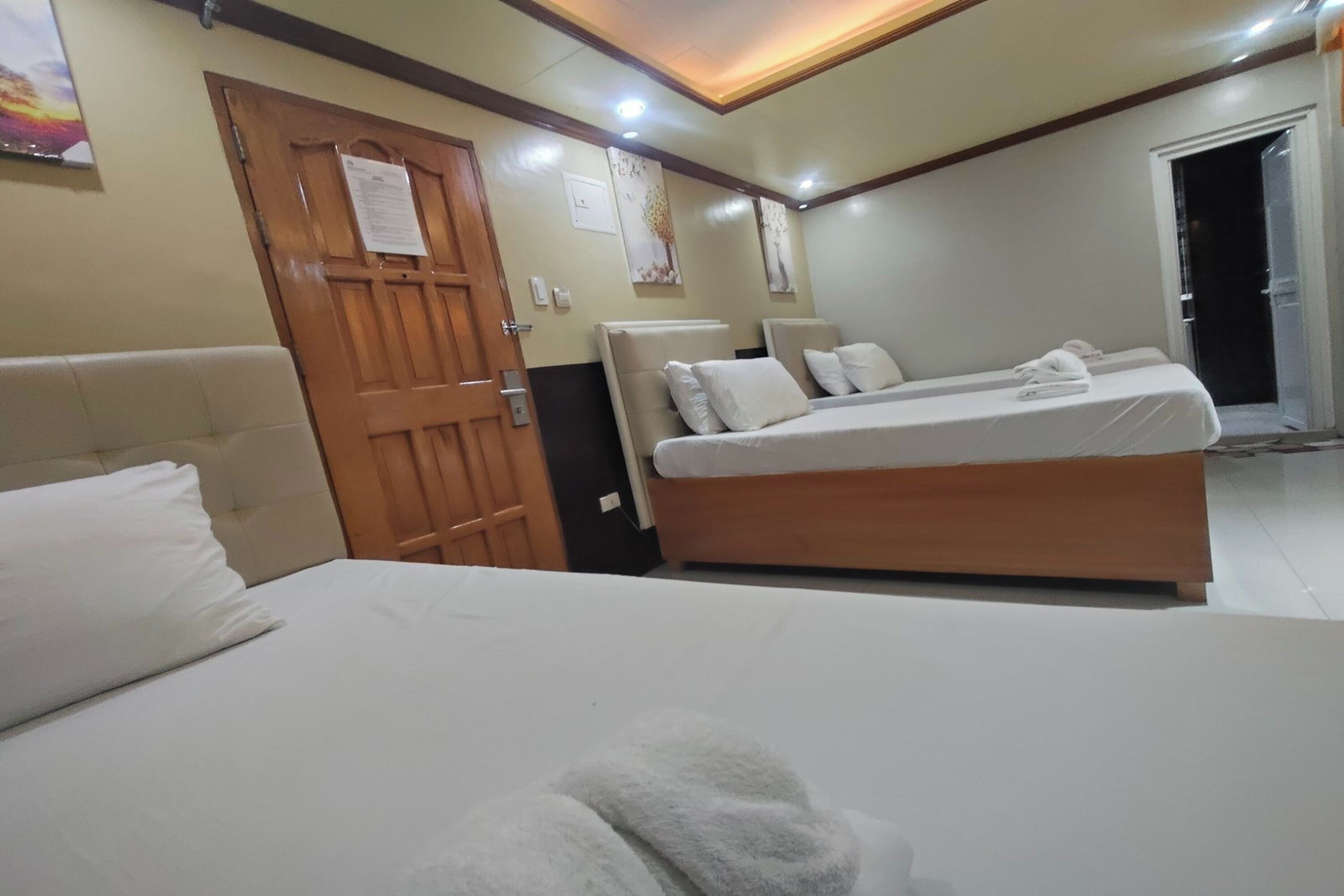 Ein Hotelzimmer mit einem großen Bett, einem kleineren Bett, einer Holztür und einem sichtbaren Badezimmer durch eine geöffnete Tür.