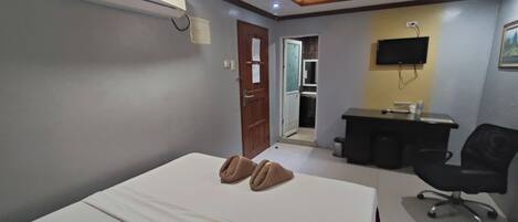 Una habitación de hotel con una cama, un escritorio, una silla, aire acondicionado y una televisión.
