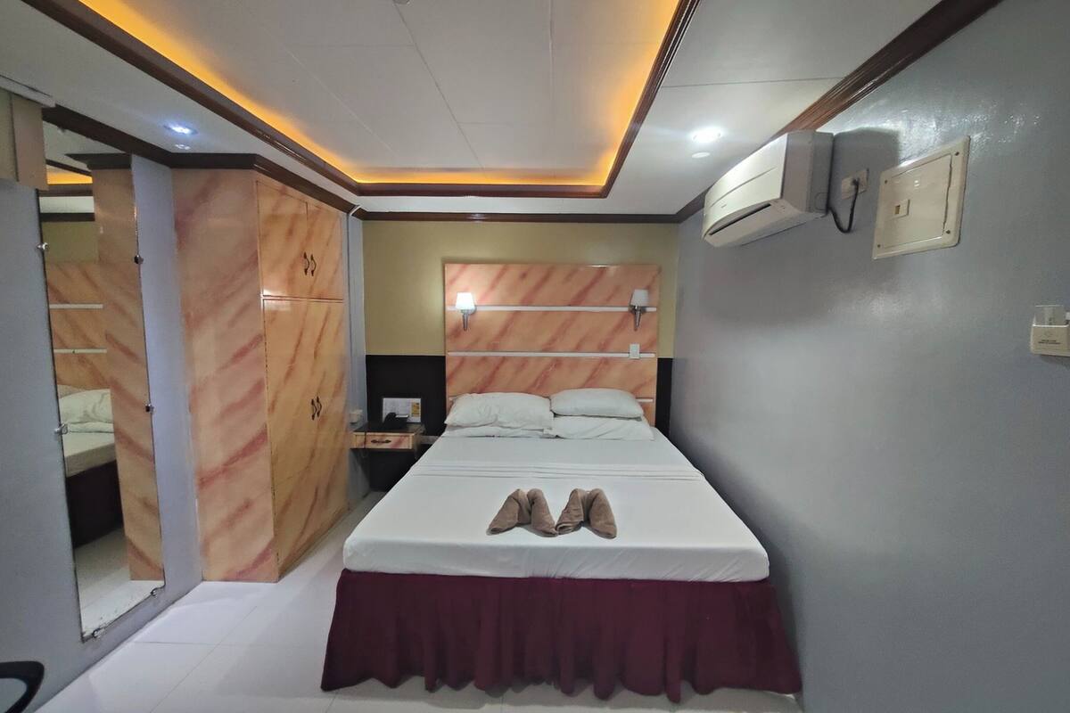 Une chambre d’hôtel équipée d’un lit, d’une armoire, d’une table de chevet et d’un climatiseur fixé au mur.