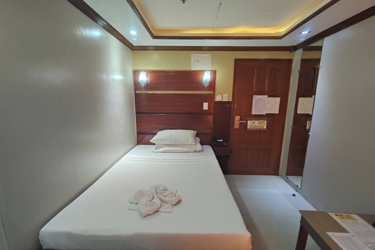 Un lit simple avec un matelas blanc, une tête de lit en bois et une paire de serviettes posées sur le lit.