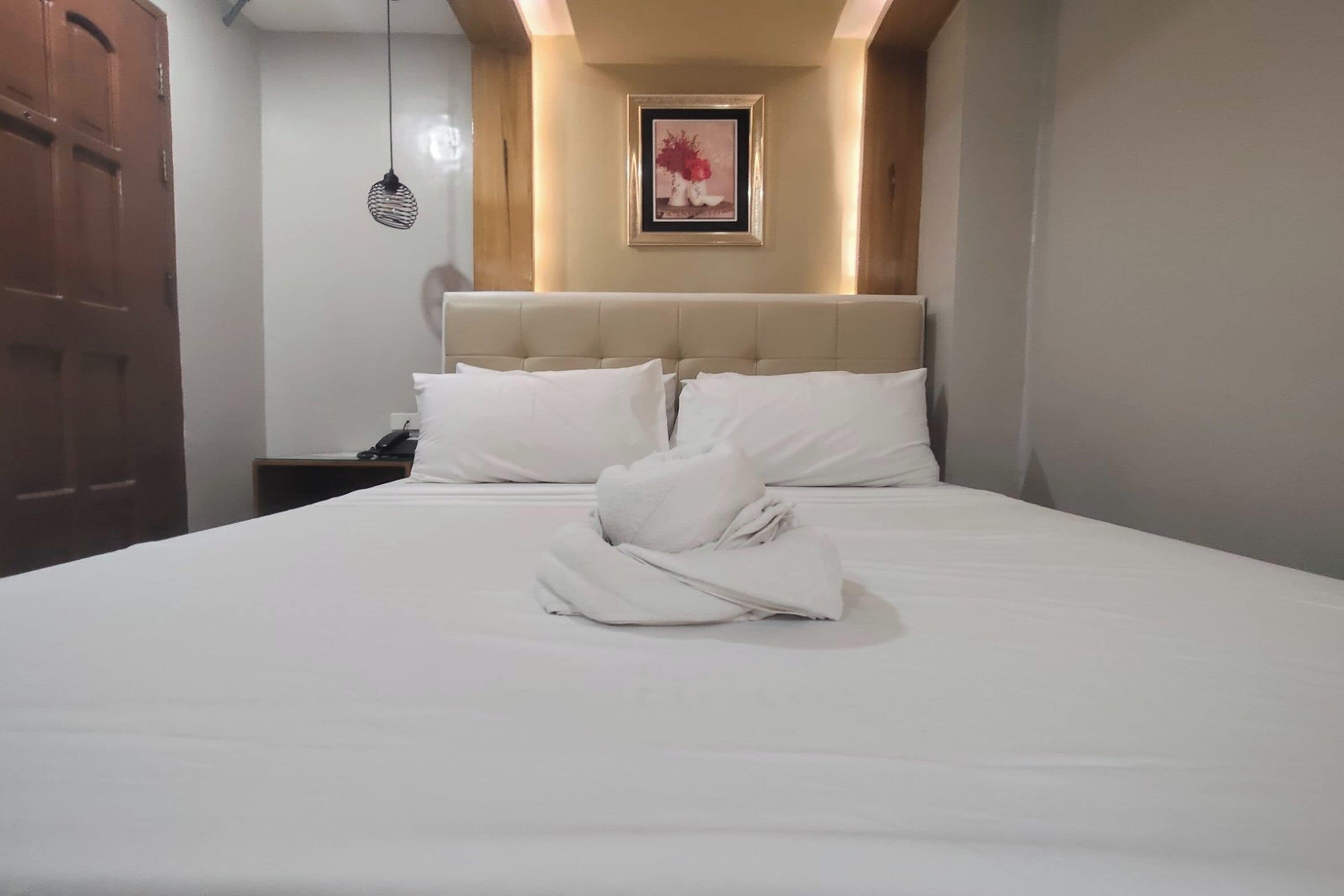 A neatly made bed with white linens and a folded towel in the center.
