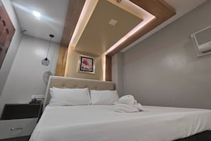 Una habitación de hotel con cama, mesita de noche y aire acondicionado instalado en la pared.
