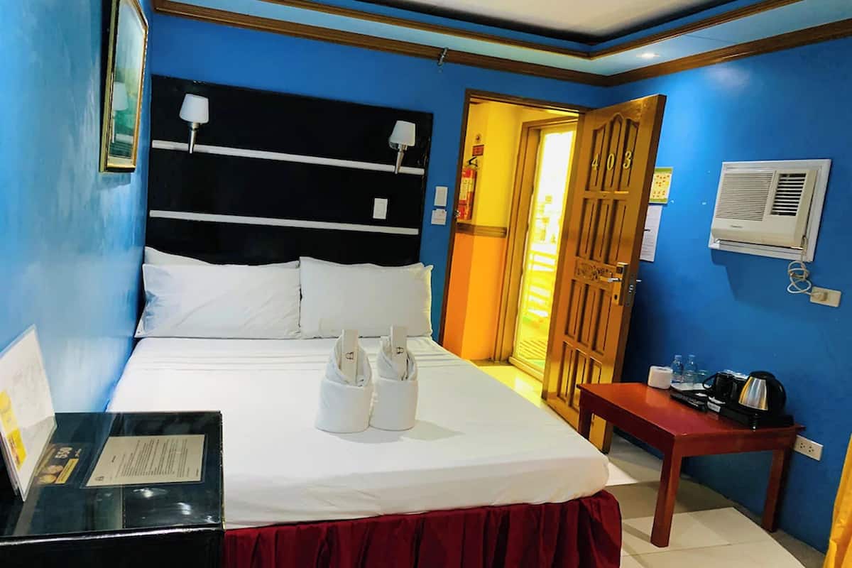 Une chambre d’hôtel avec un lit, un bureau, un rideau rouge, une porte en bois et un climatiseur fixé au mur.