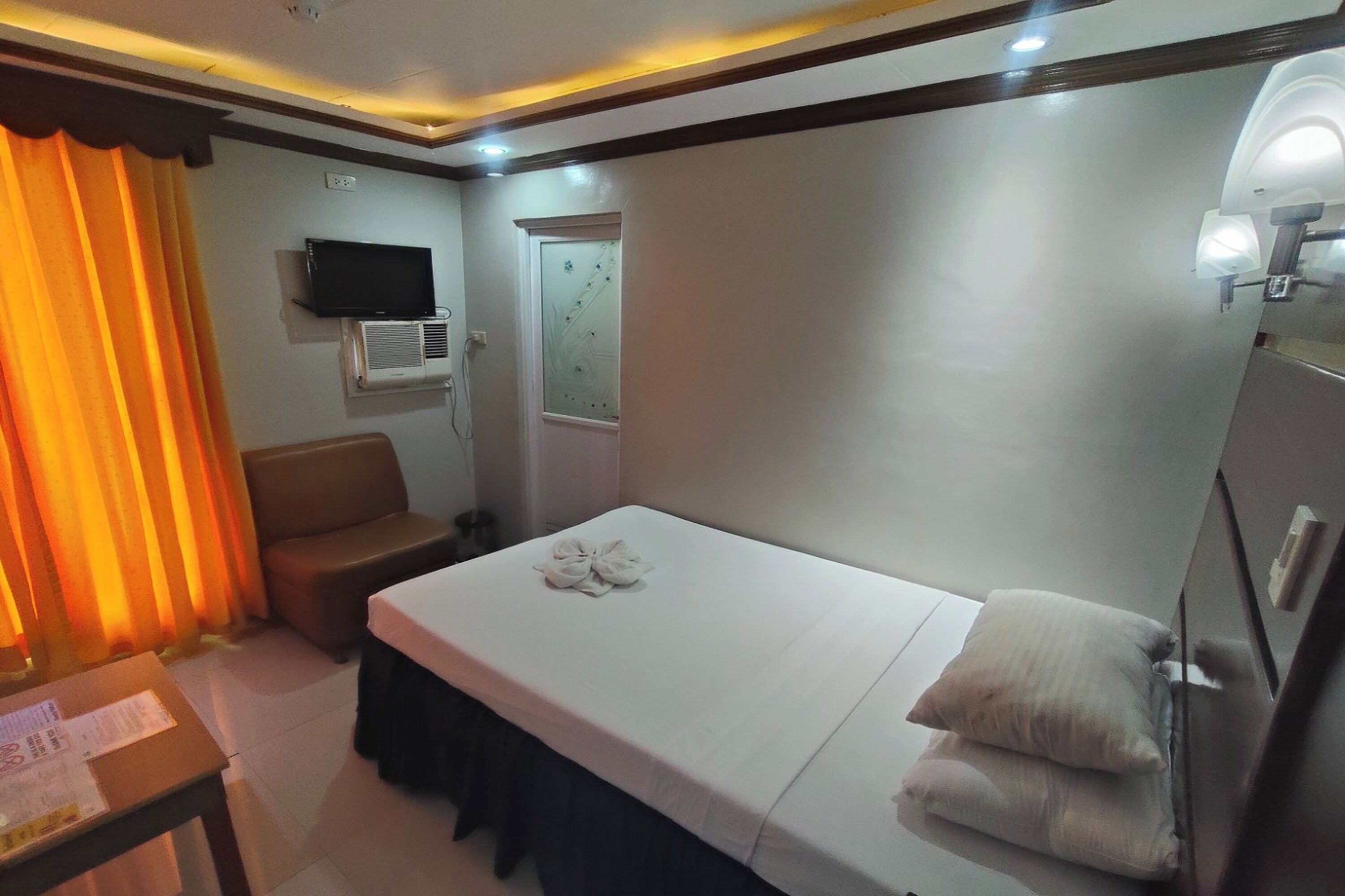 A hotel room with a bed, a chair, a television, and an air conditioning unit.