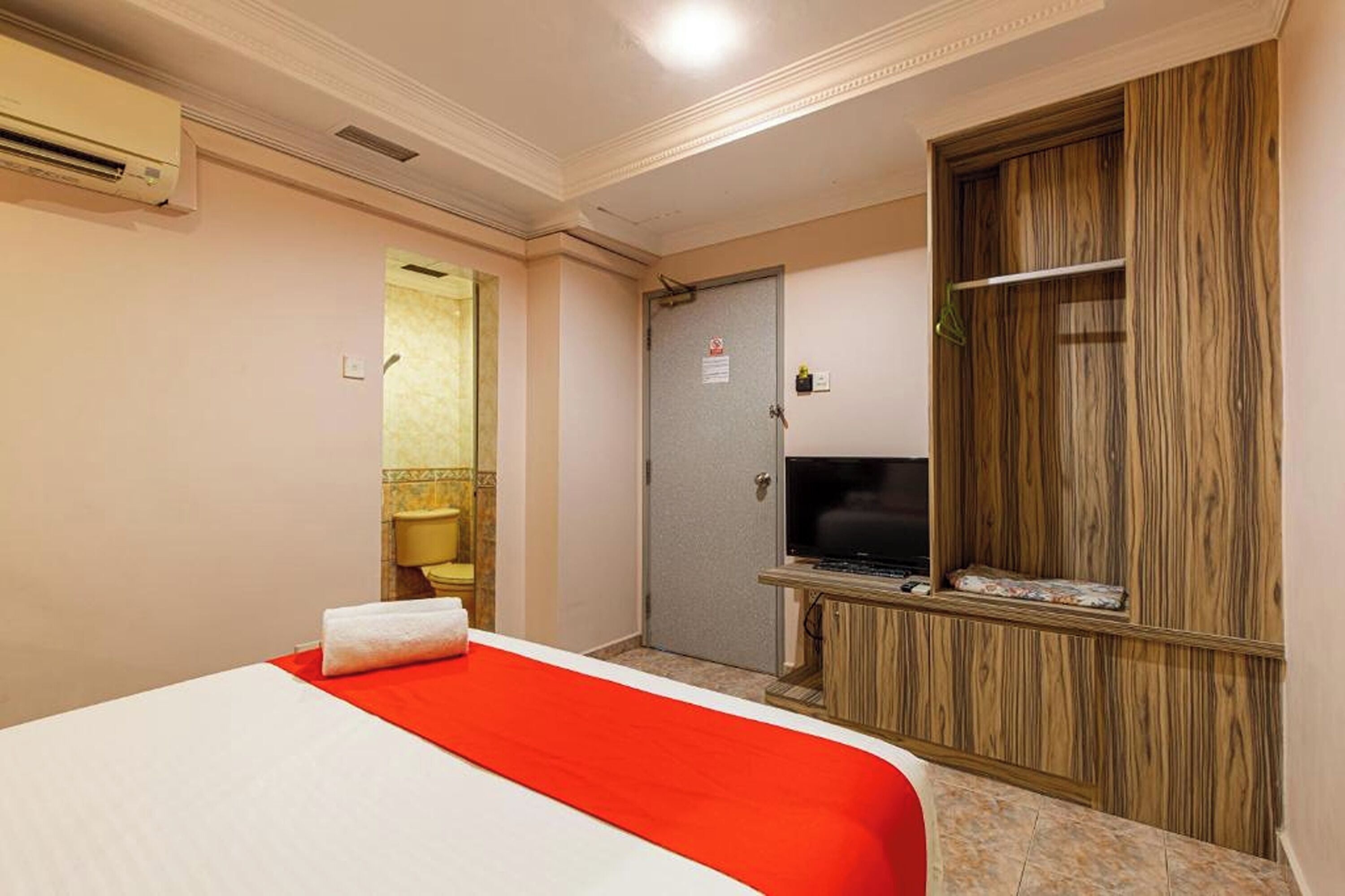 Une chambre d’hôtel avec un lit, une télévision, une armoire et une salle de bain visible à travers une porte ouverte.