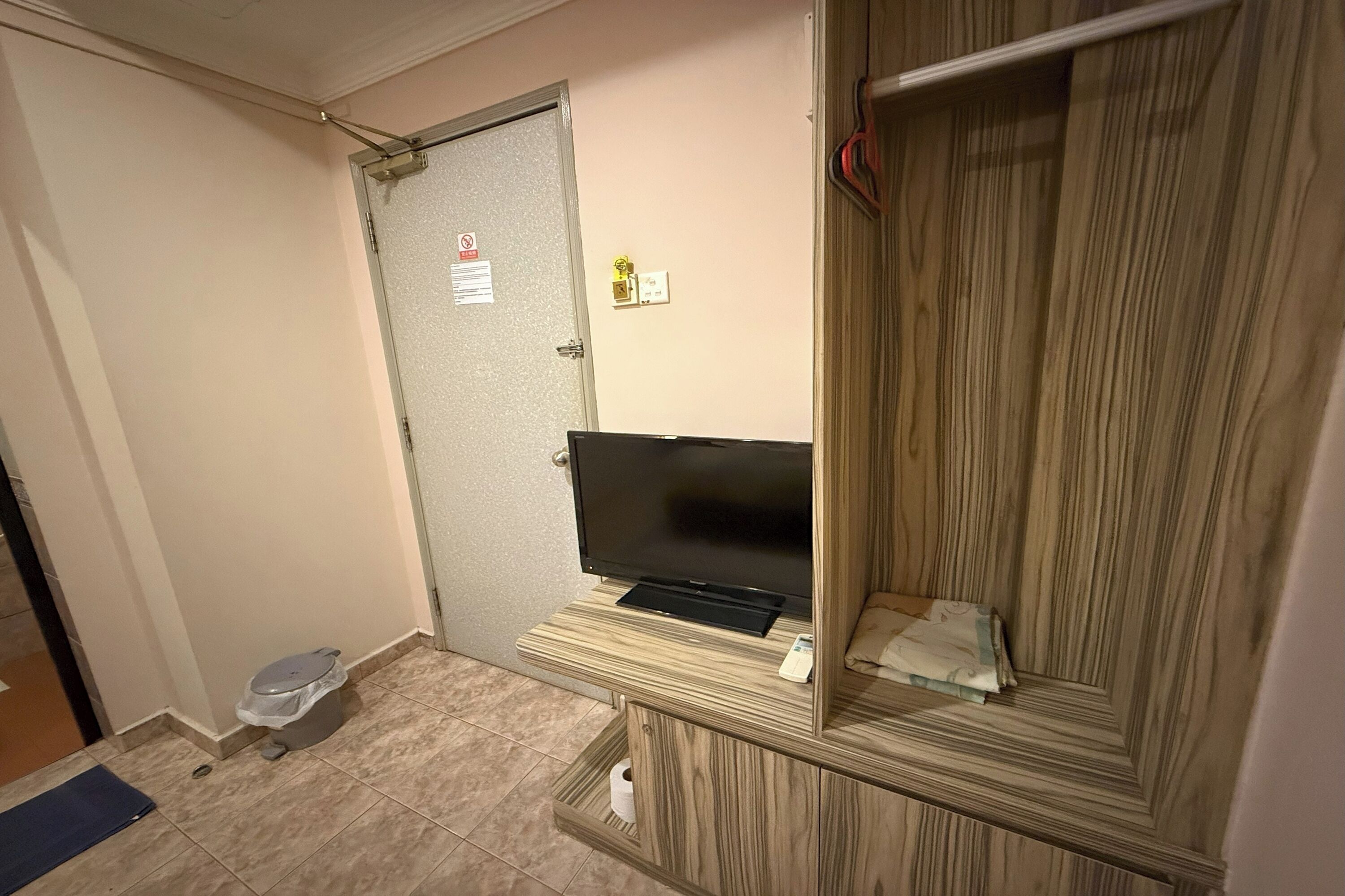 A bathroom with a toilet, a shower area, a television on a wooden shelf, and a towel rack.