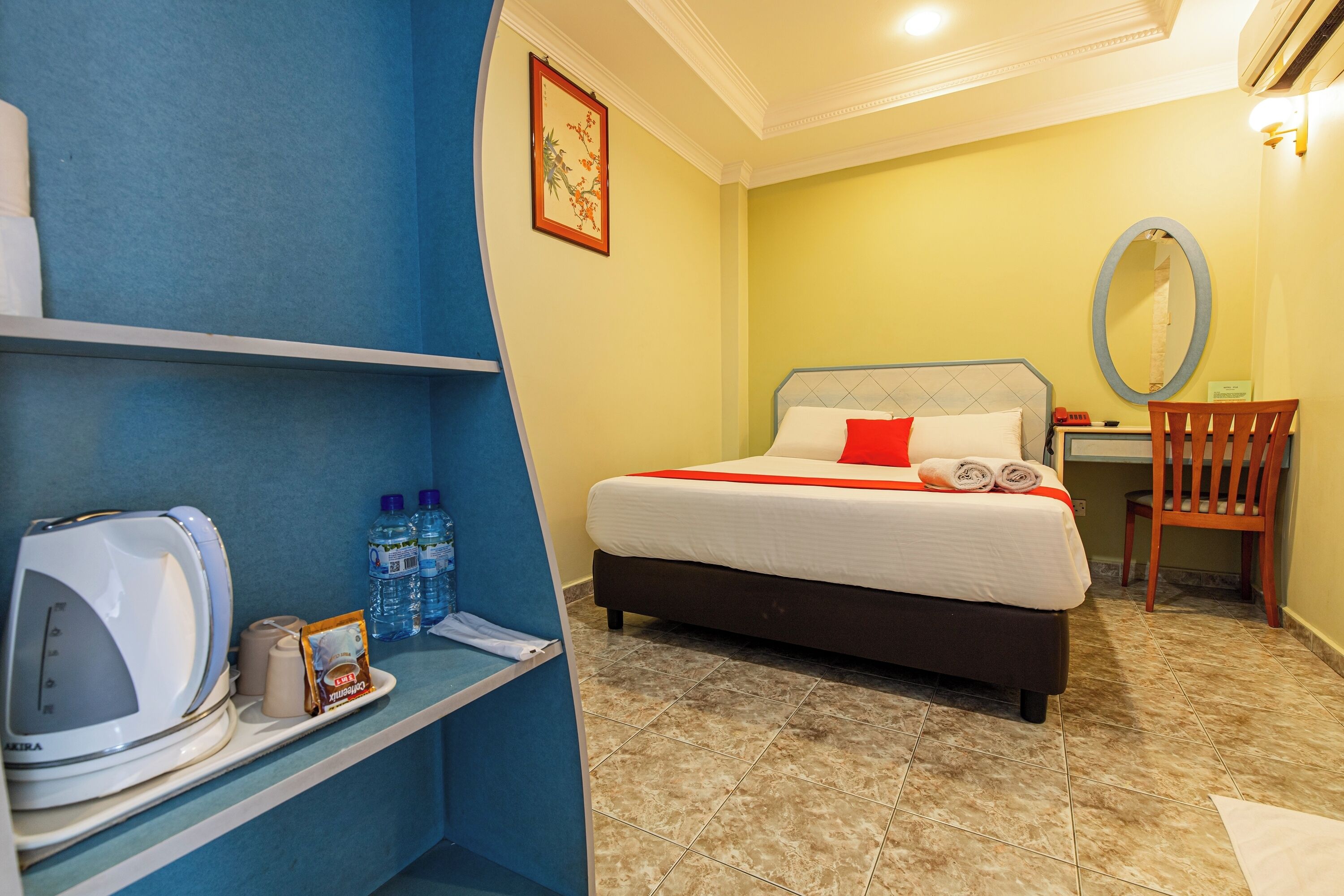 Habitación de hotel con cama, una silla, escritorio, repisa con artículos de tocador y espejo montado en la pared.
