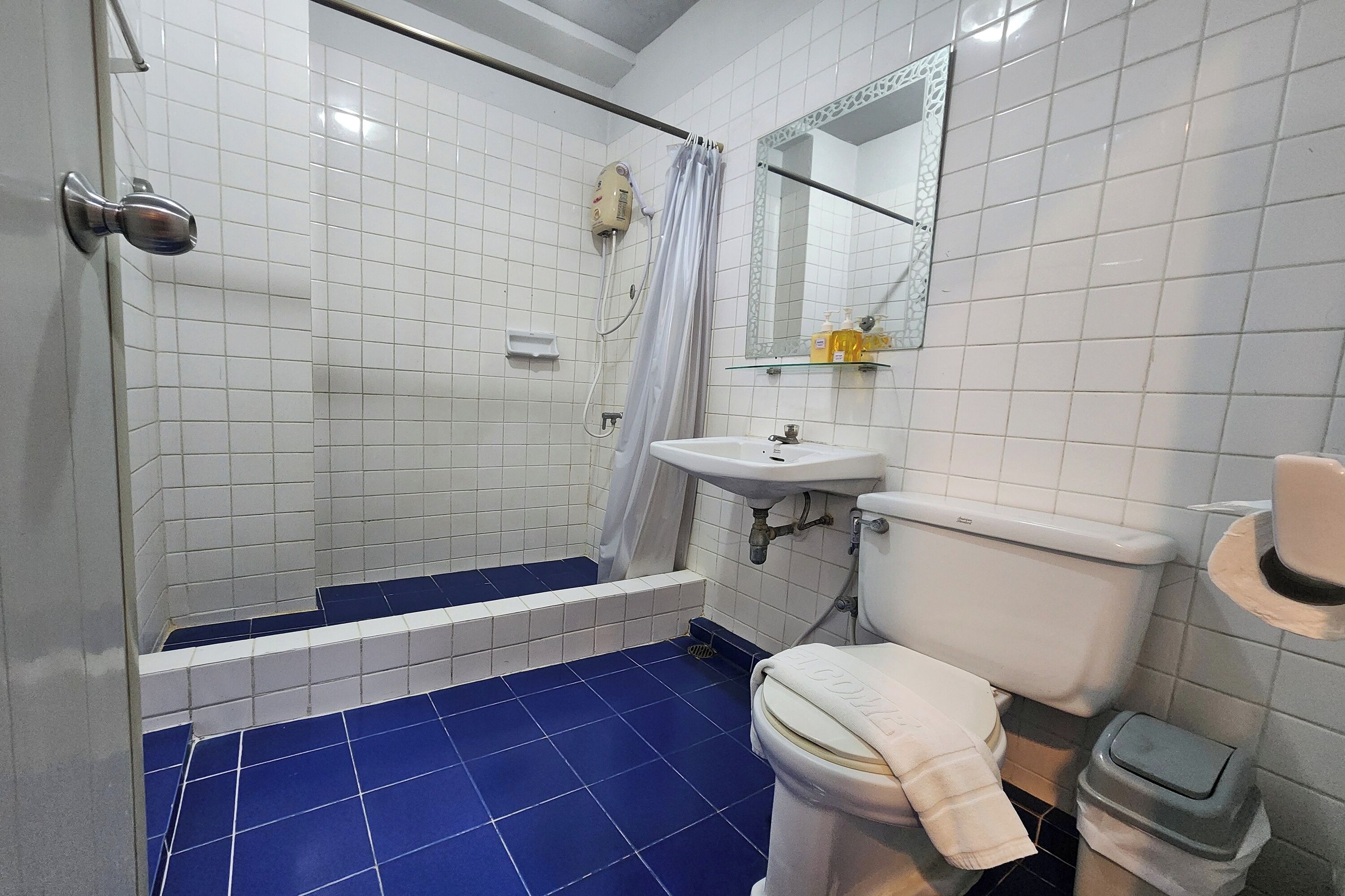 A bathroom with a shower, toilet, sink, and tiled floor.