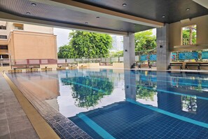 Una piscina con agua cristalina, solárium con azulejos y bancos.